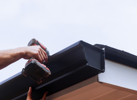 Up close image of a hand installing a new gutter with a drill