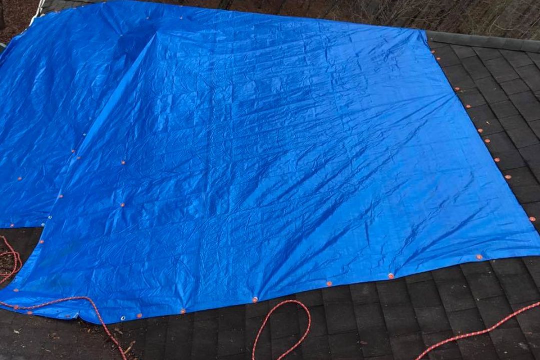 Photo of a tarp covering a shingled roof by insurance claim roofers