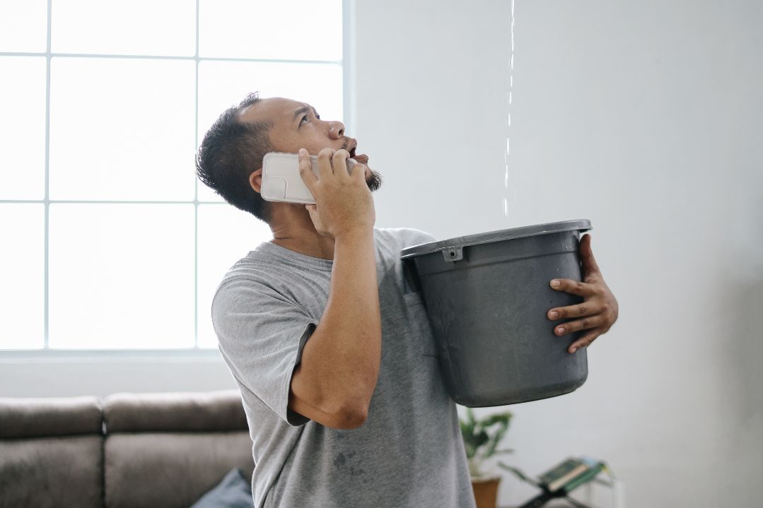 home needing roof leak repair and someone catching water leak with bucket