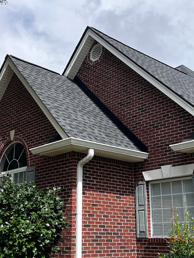 New cheap roof installed on house. Gray asphalt shingles on a brick house.