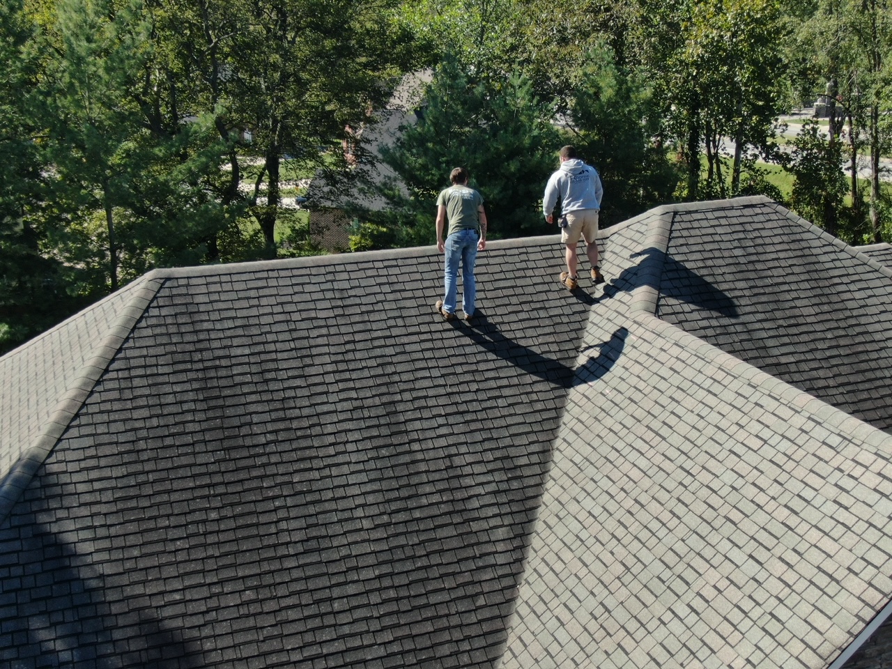 Two roofers on a home with brown shingles before rooftop repairs