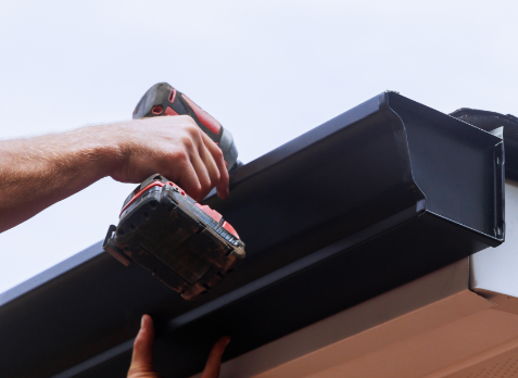 Up close image of a hand installing a new gutter with a drill