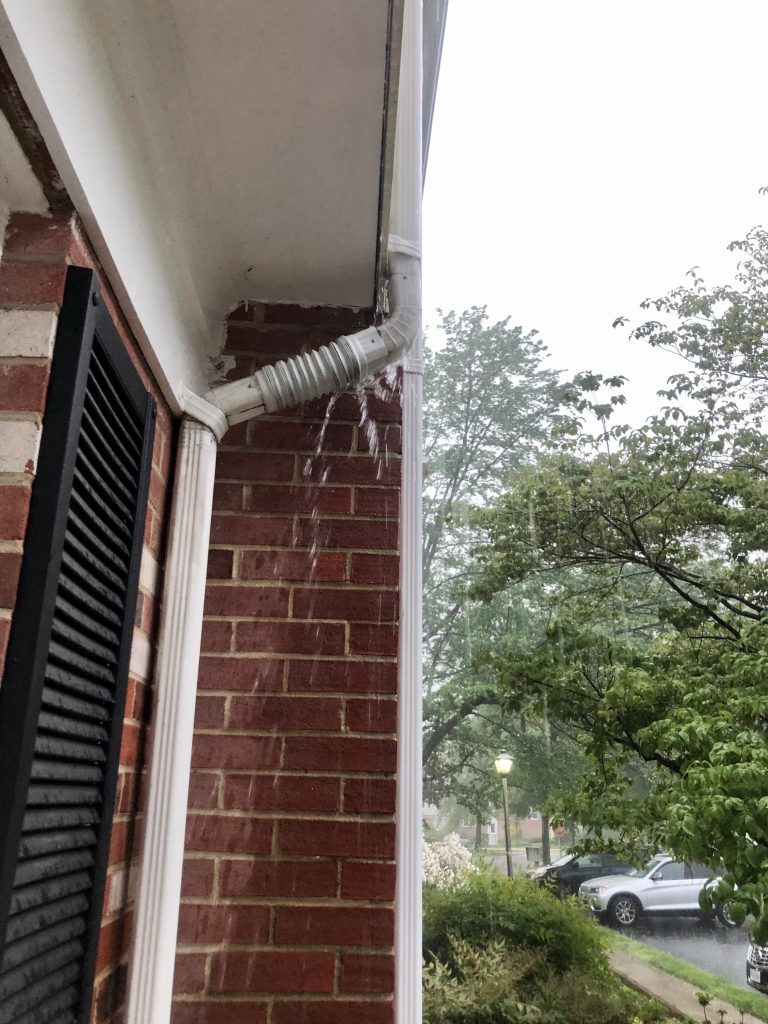 Upclose photo of a damaged downspout on a home overflowing with rainwater