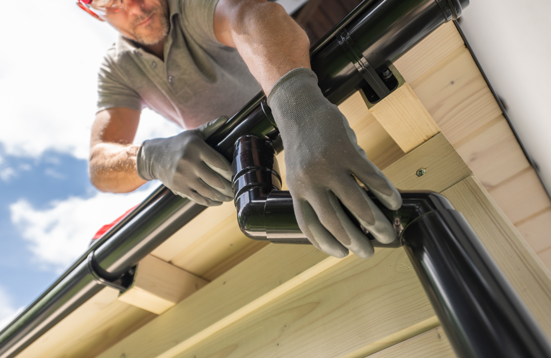 Photo of a roofer installing new black Gutters and downspouts