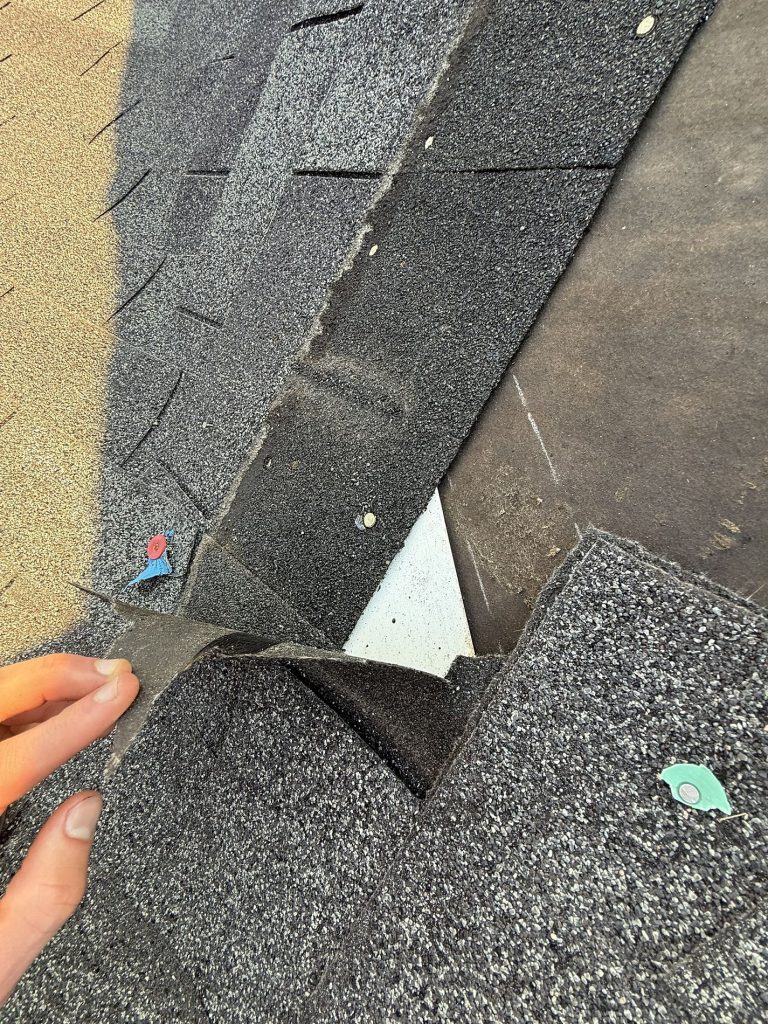 Upclose image of a hand peeling back and revealing asphalt shingle damage