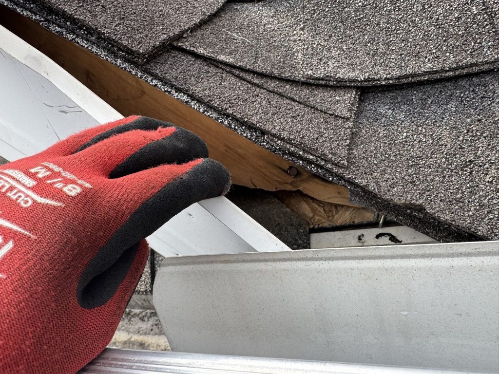 upclose image of a hand revealing wood damage behind a fascia board.