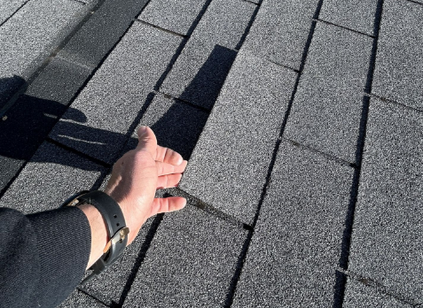 Image of a roofers hand inspecting a residential shingle roof during a roof inspection