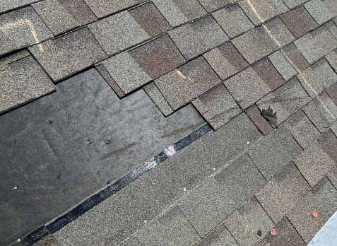 Close up image of gray roof with missing asphalt shingles after storm damage