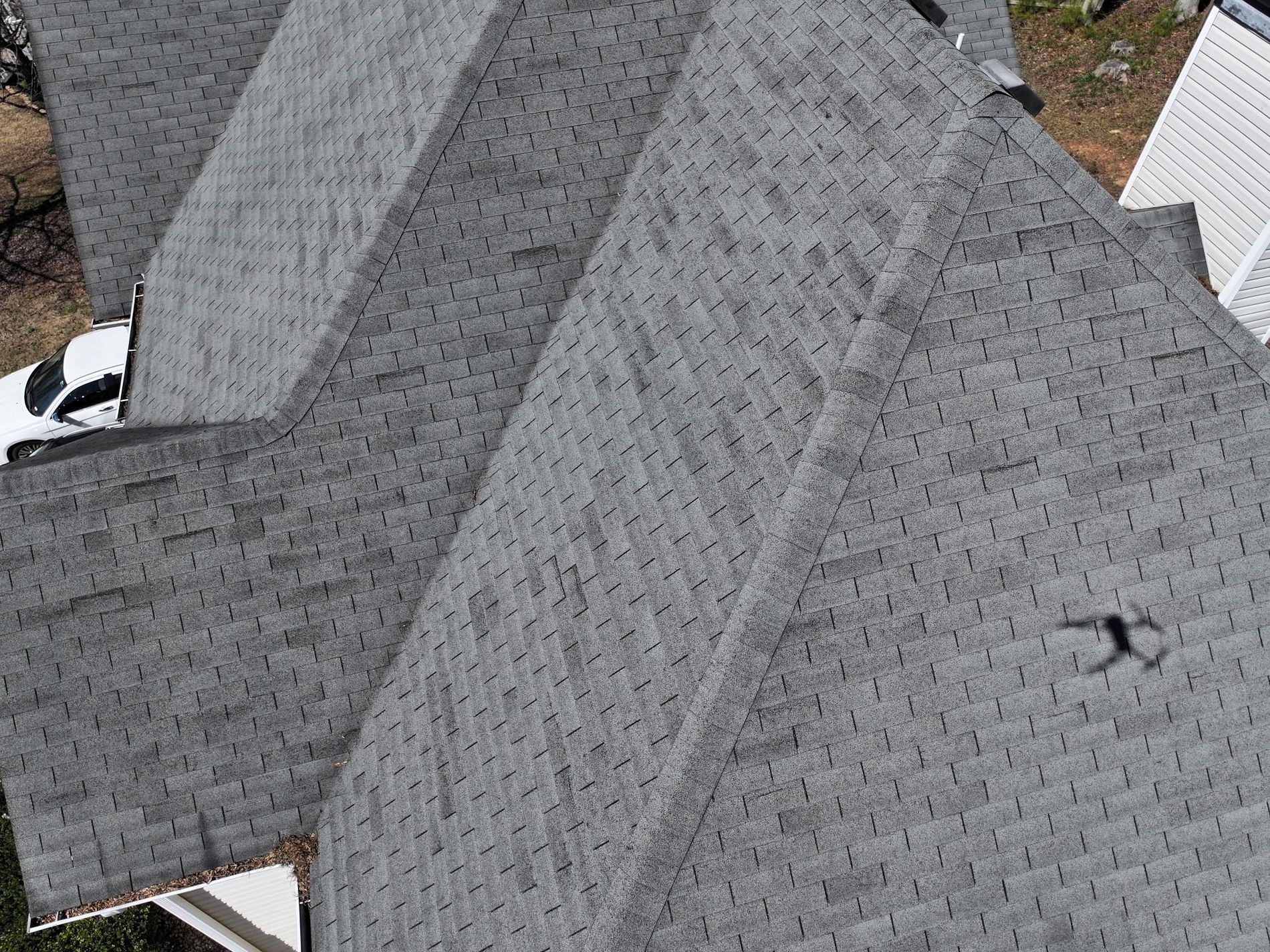 Aerial photo of hail damage roofing contractors inspecting a gray shingle roof after hail storm with drone