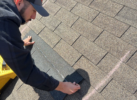 Photo of a roof contractor on roof replacing some damaged asphalt shingles