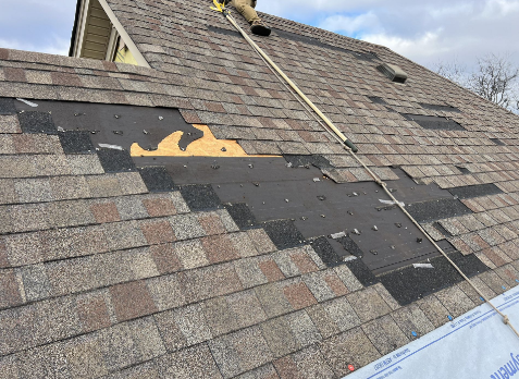 Close up image of gray roof with missing asphalt shingles after storm damage