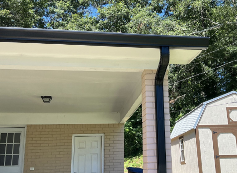 Photo looking up at new black Gutters and downspouts on the right corner of a home