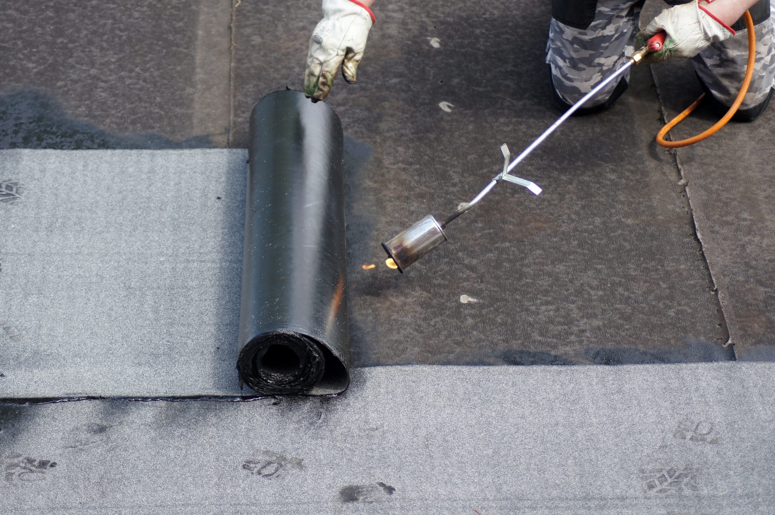 Flat roof installation with propane blowtorch during construction works with rolled roofing