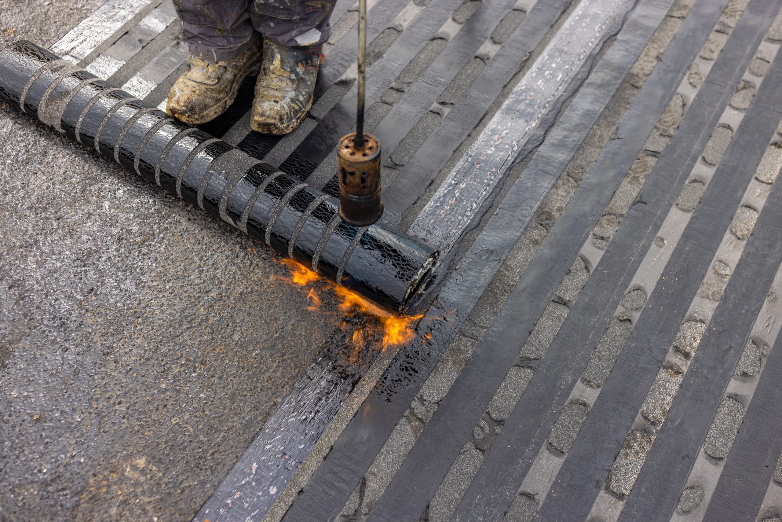 Workers installing rolled roofing on the roof using a propane gas