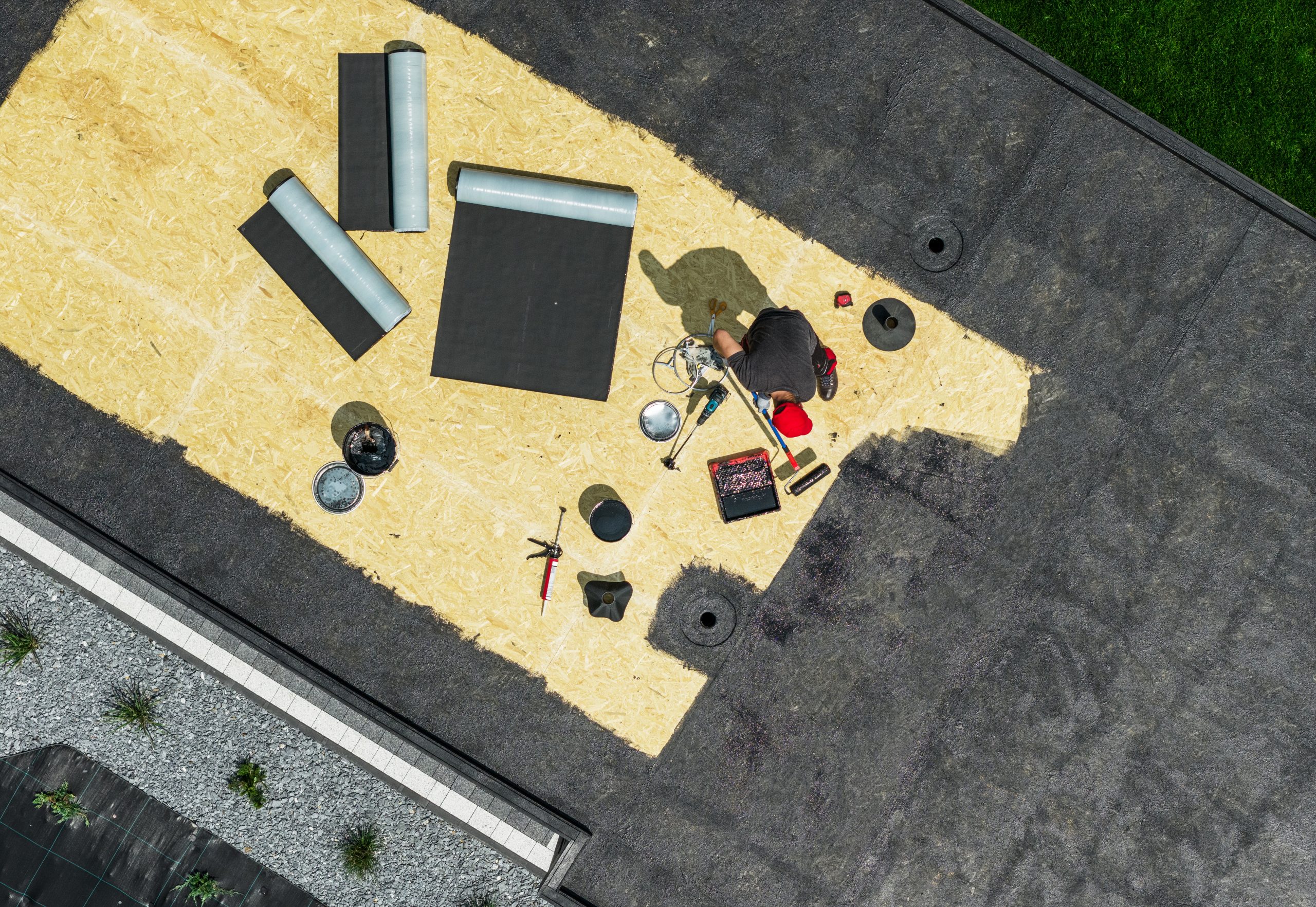 A worker repairs a flat roof in a sunny environment using various tools and materials.