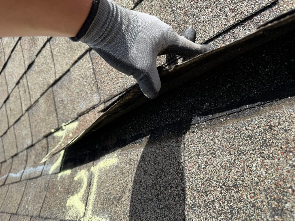 hand with glove on inspecting a damaged shingle on a roof in birmingham