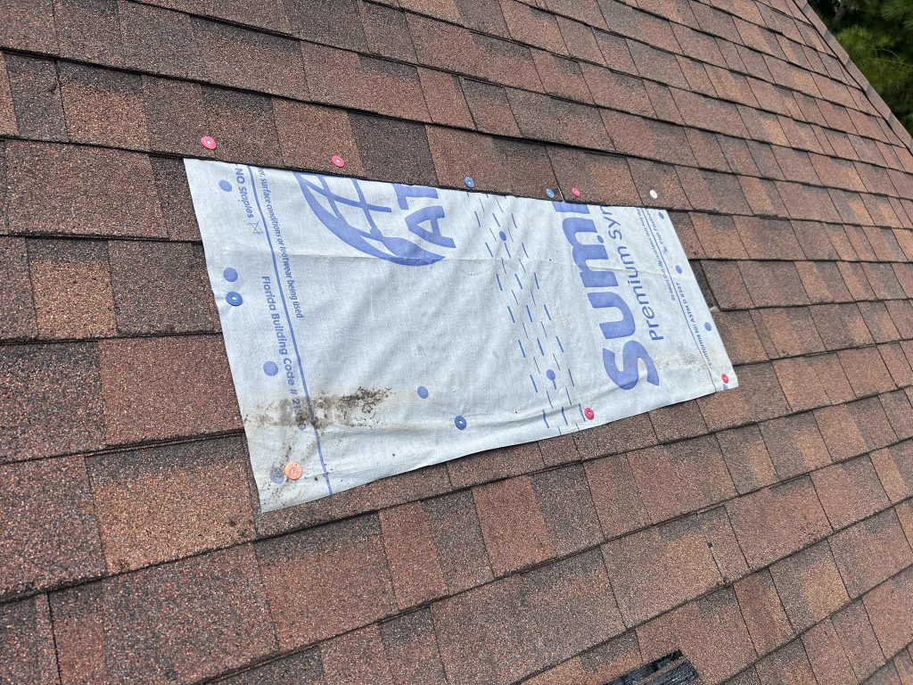 Close up image of an asphalt roof with a tarp over some damaged shingles before a roof repair in birmingham.