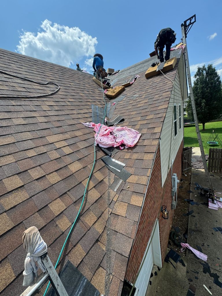 Roofers on roof installing new asphalt shingles after storms left behind roof leaking damage.