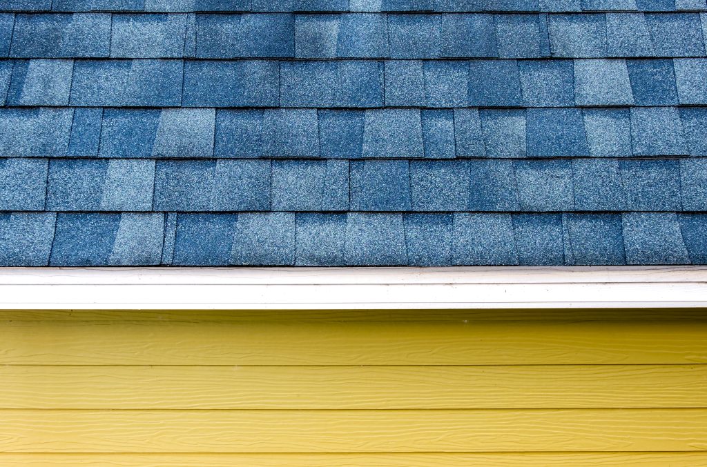 close up roof with architectural shingles and yellow wooden plank wall
