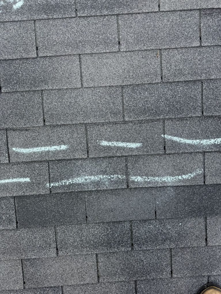 Photo from a roofer on a roof showing a shingle that has been torn off due to wind damage.