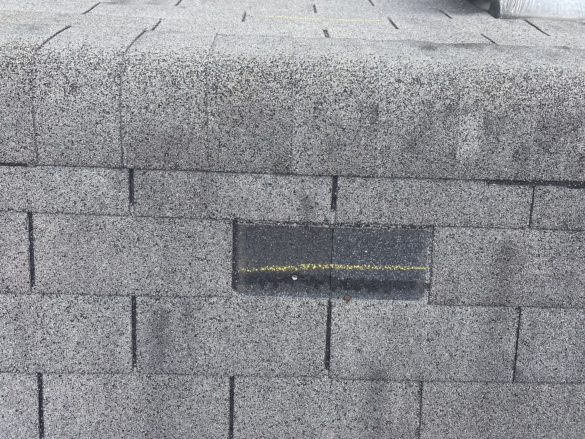 Photo from a roofer on a roof showing a shingle that has been torn off due to wind damage.