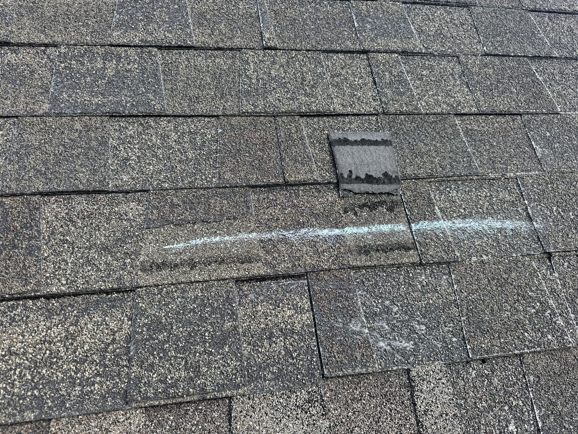 Photo from a roofer on a roof showing a shingle that has been torn off due to wind damage.