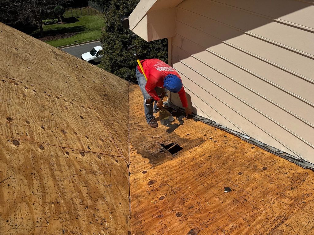 Photo of a roofer repairing a wind damage roof that led to a water leak and a hole in the roof.