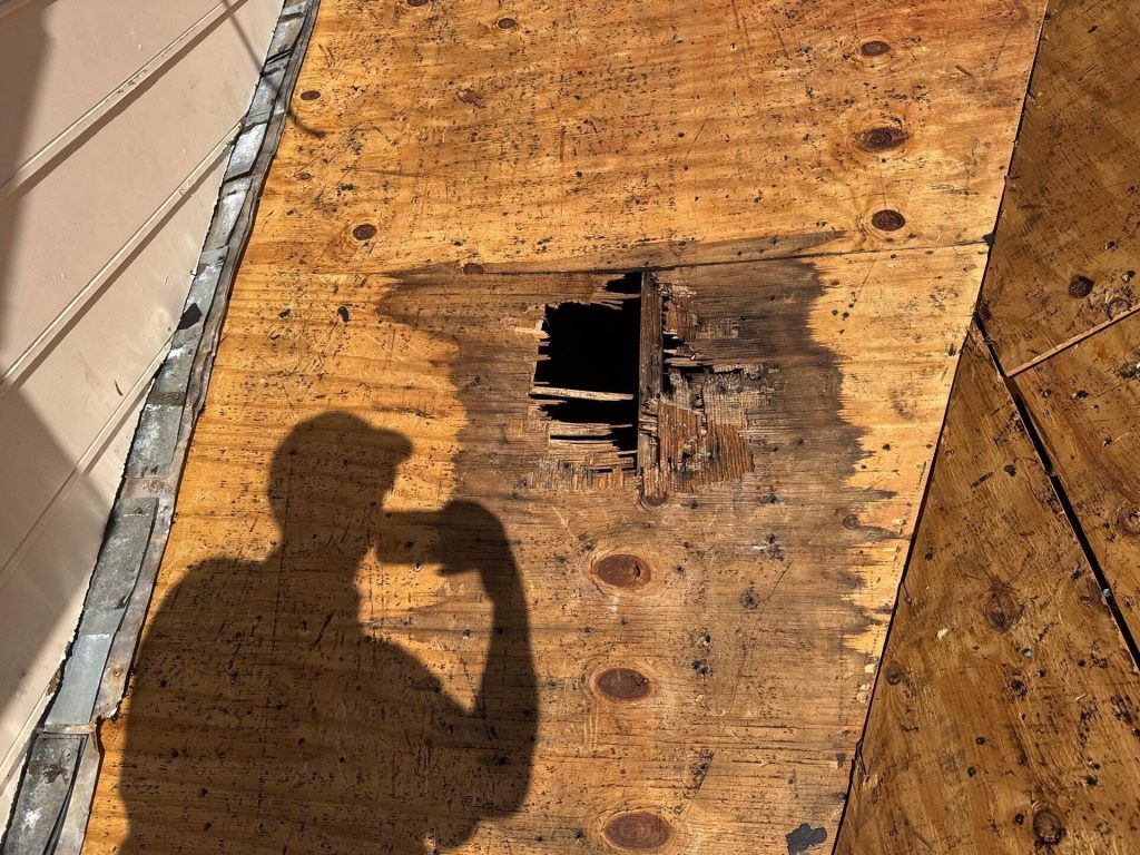 Image of a hole on a sheet of OSB on a roof after removing the shingles that was caused by wind damage to roof.