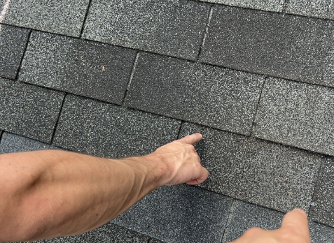 Image of a roofers hand inspecting a residential shingle roof during a roof inspection in Anniston Meade.