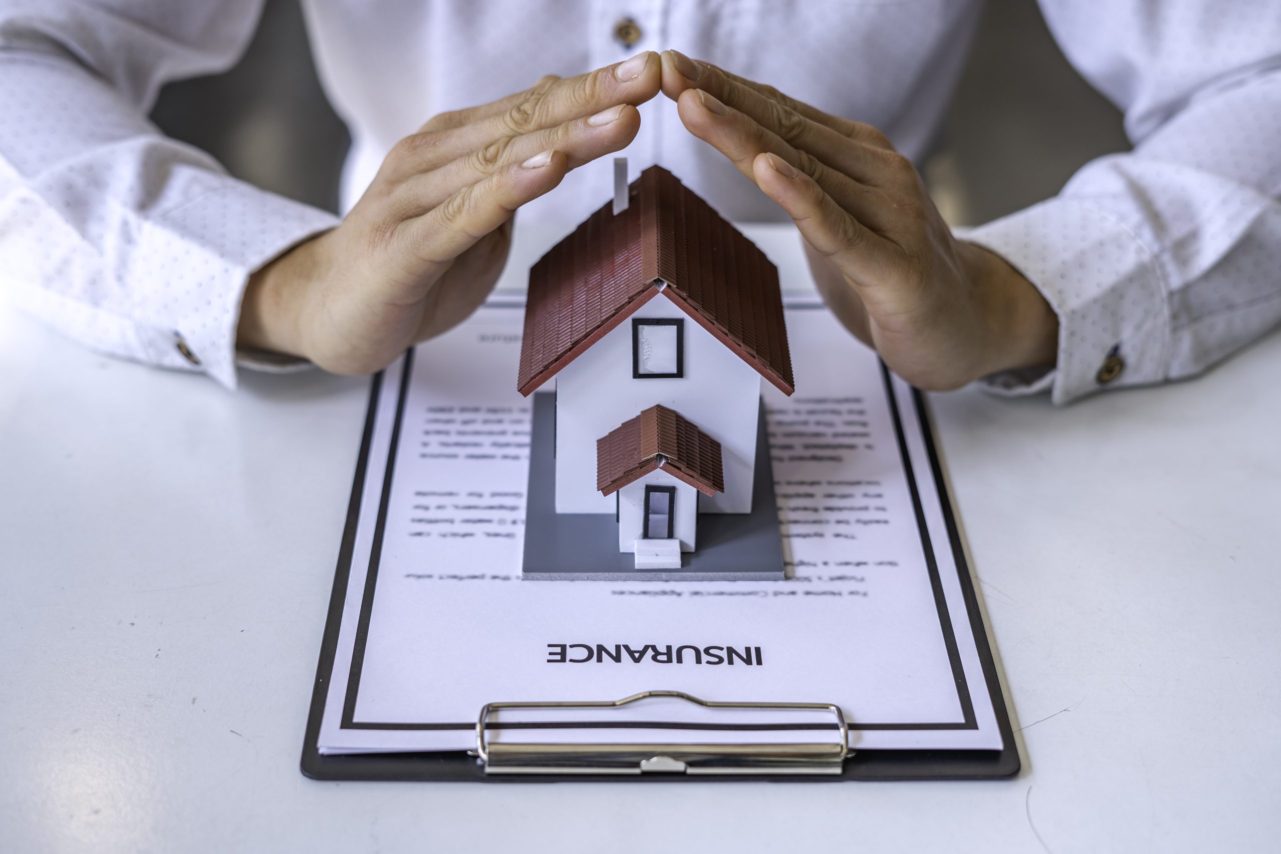 Home security and roof insurance concept - A close-up view of a man defending a home model by hand on a table in an office. And are explaining the agreement to the customer